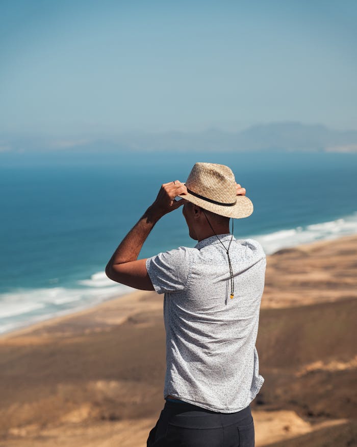 Man in straw hat gazes at expansive coastline on a sunny day, capturing serene outdoor exploration.