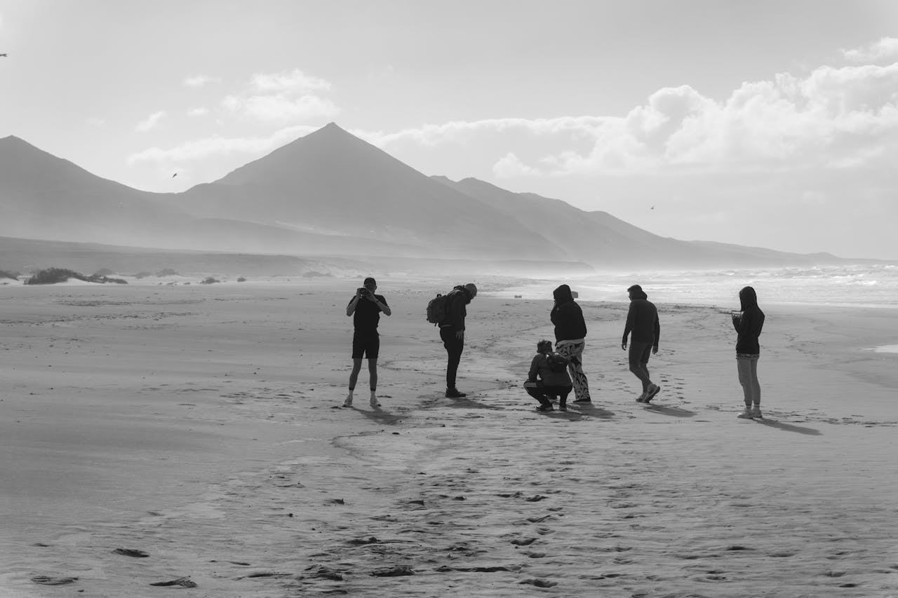 A group of people enjoys a sandy beach with mountains in Fuerteventura, Spain.